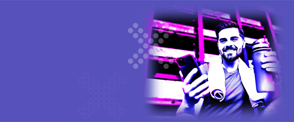 A man with a beard is holding a phone in front of a purple background.
