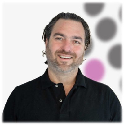 A man smiling in front of a polka dot background.