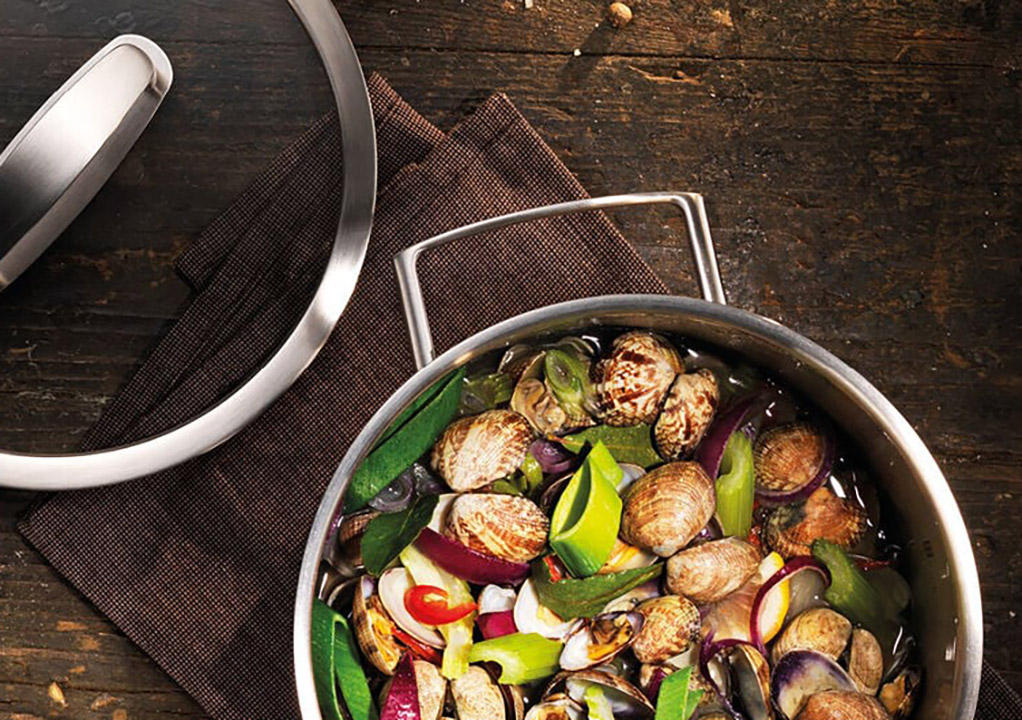 A pan filled with vegetables and a pot on a table.